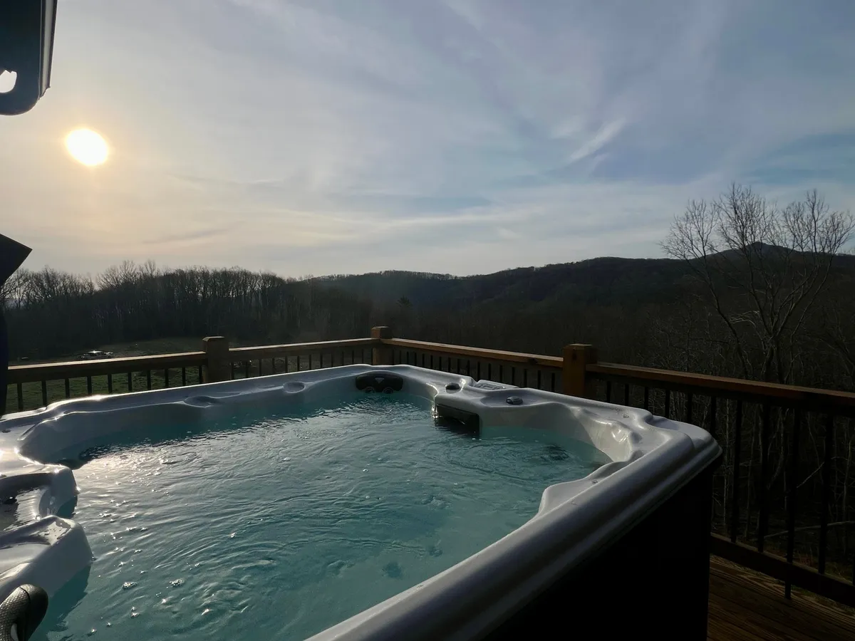 An outdoor hot tub set on a wooden deck, overlooking sweeping mountain views and a spectacular sunset. The tranquil atmosphere is accented by the warm glow of dusk, suggesting moments of relaxation and enjoyment after a day spent touring vineyards.