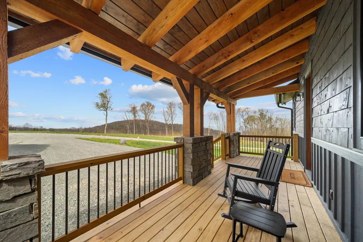 A peaceful porch scene with classic rocking chairs, sturdy stone columns, and wooden beams, situated to look out over serene natural surroundings. The setting suggests quiet mornings or evenings spent connecting as a family while enjoying the outdoors.