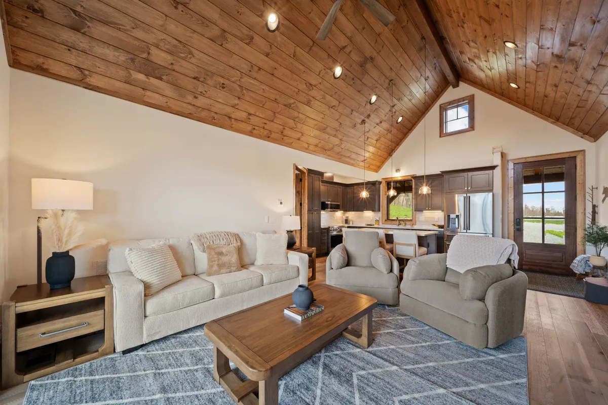 This image provides a view into the open living area with a plush sofa, coffee table, kitchen area, and visible wooden ceiling. The front door and open sightlines underscore the welcoming, communal vibe and the home’s flexible setup for hosting guests or relaxing family nights.