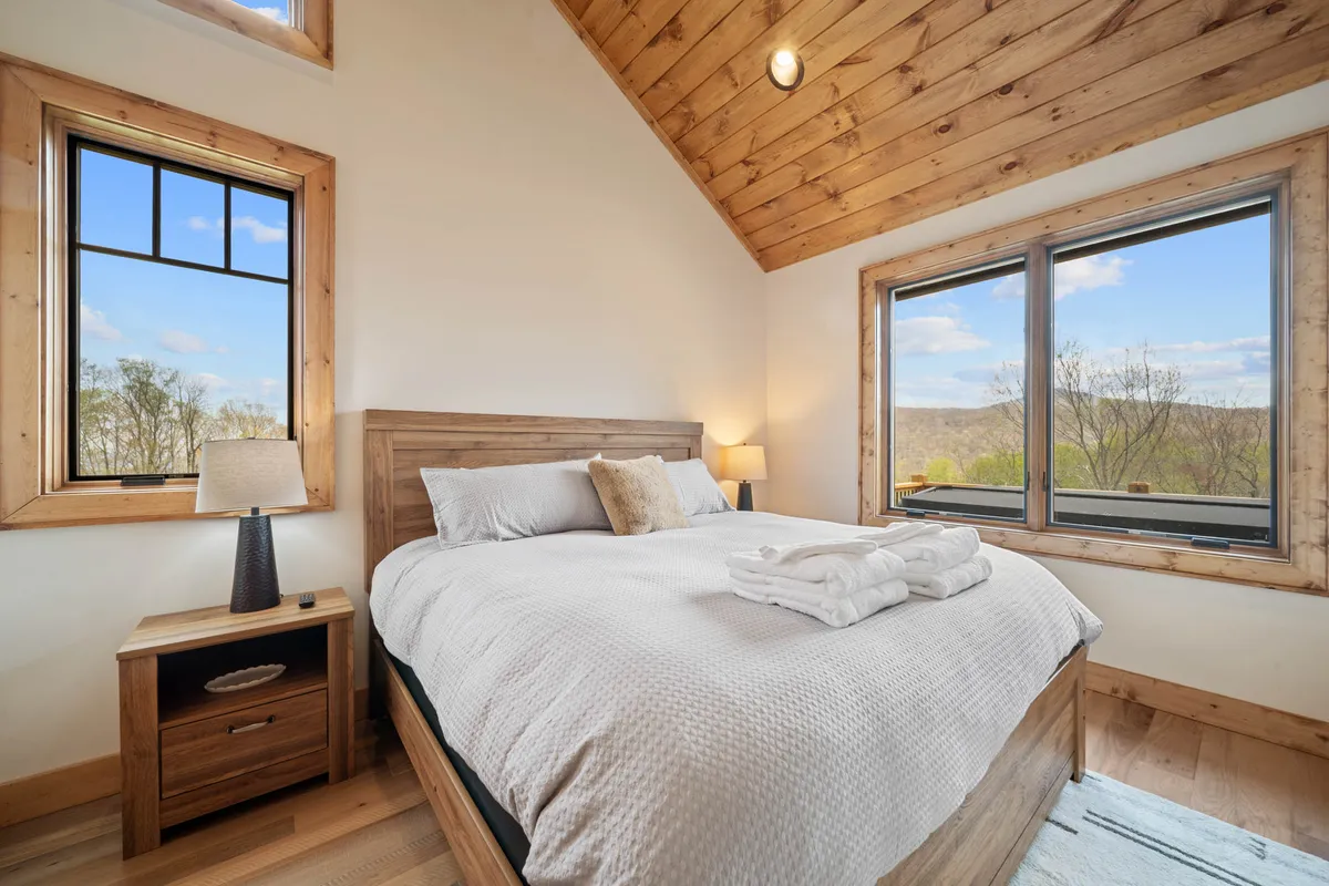 A cozy king suite featuring a plush bed with crisp, comfortable linens and large windows that allow natural light to flood the room. Wooden accents lend a warm, inviting feel while the mountain landscape outside enhances the sense of escape.