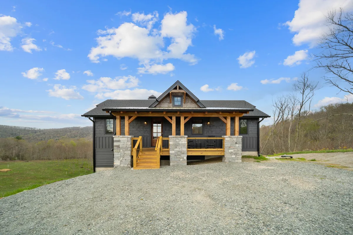 A welcoming exterior porch featuring wooden beams and sturdy stone pillars, with comfortable seating inviting guests to relax. The porch looks out over natural surroundings, creating an ideal spot for sipping wine or enjoying a leisurely brunch while taking in the High Country ambiance.