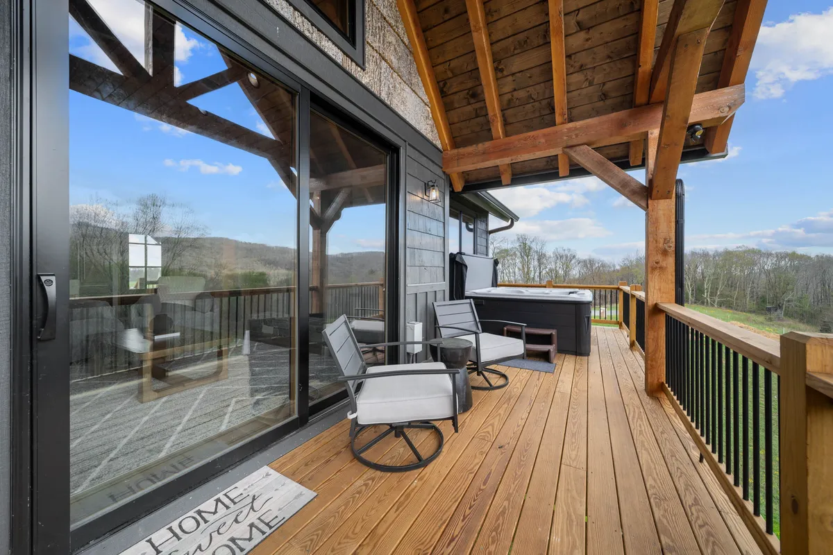 A serene exterior deck space with a hot tub and comfortable outdoor seating, surrounded by natural foliage. The space is set up for both relaxation and socializing, with views that showcase the region's natural beauty and changing seasons.