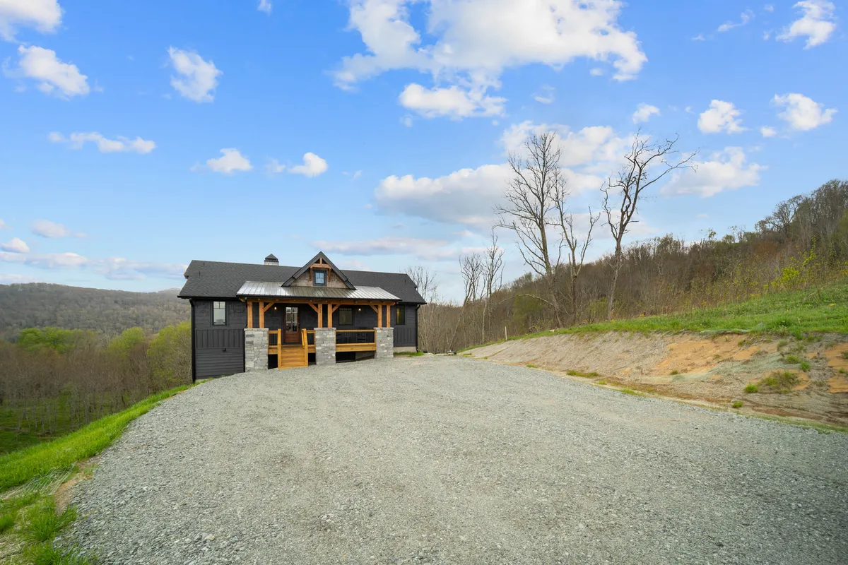 A wide-angle view of the house sits amidst a tranquil landscape, showcasing the home’s exterior, driveway, and surrounding woods. The setting is peaceful and private, emphasizing the natural beauty and exclusivity of the gated community.