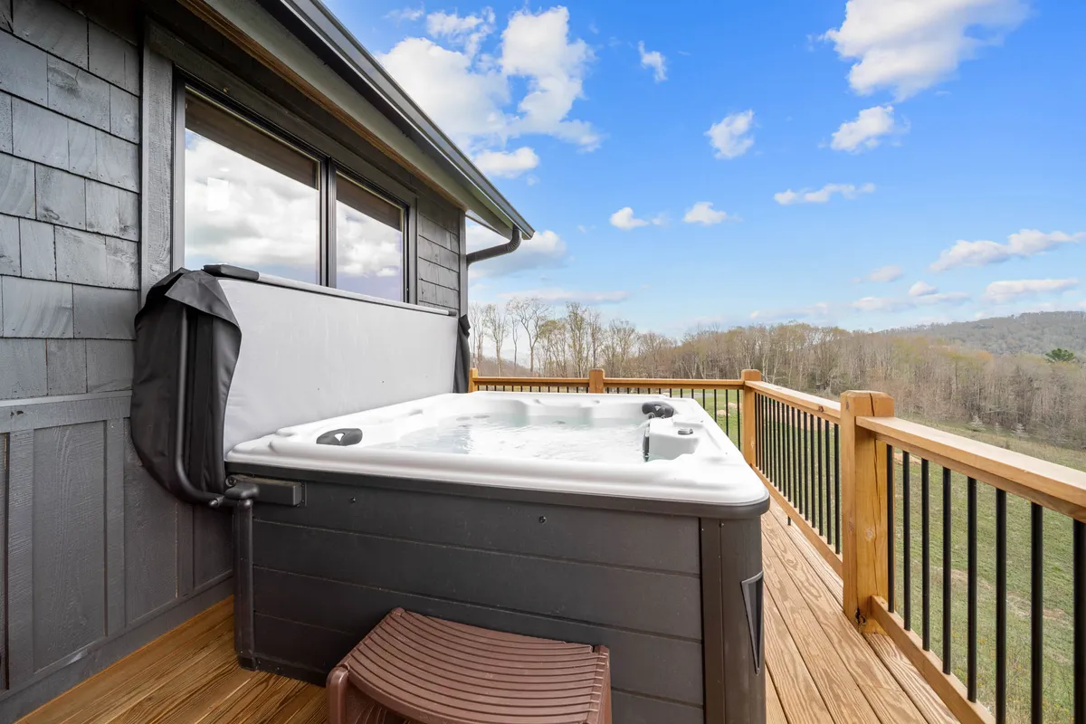 This image features a bubbling hot tub on a wooden deck, surrounded by a sturdy railing, with a beautiful natural landscape and mountains visible in the background. The scene exudes tranquility and invites guests to unwind in the serene outdoor setting.